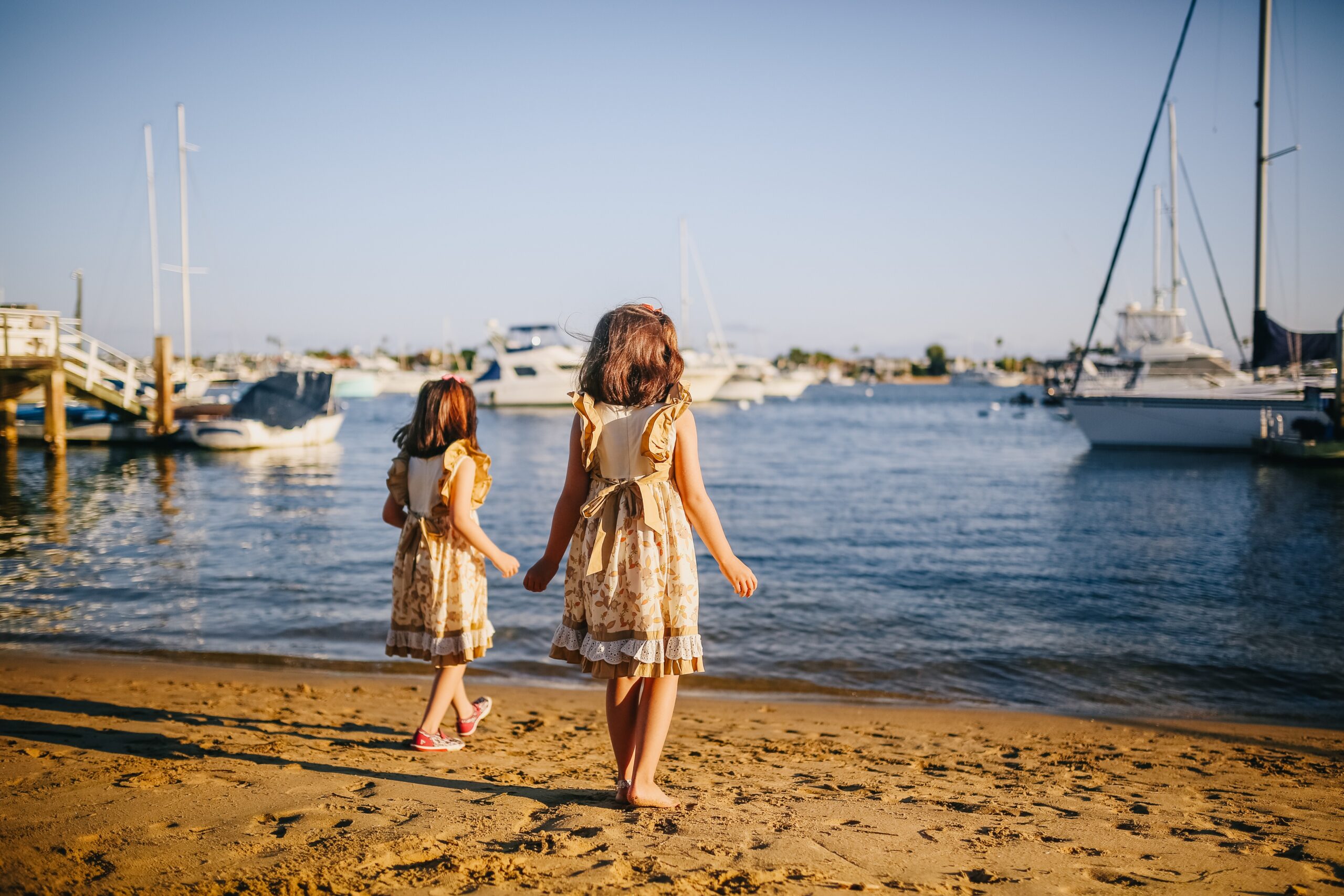 Autistic twins on vacation stand on the shore with boats in the distance
