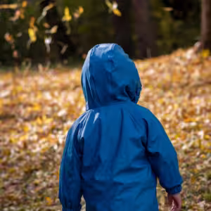 Autistic twin boy in raincoat playing in leaves.