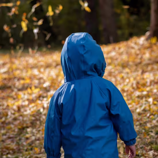 Autistic twin boy in raincoat playing in leaves.