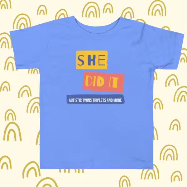 Blue t-shirt with yellow and pink writing that says "She Did It: Autistic Twins Triplets and More"