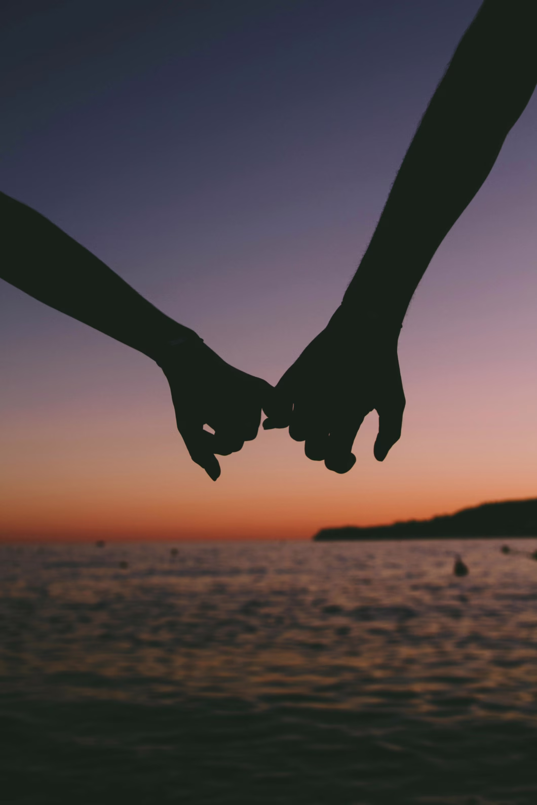 A couple holding hands in front of a beach sunset.