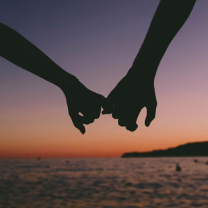 A couple holding hands in front of a beach sunset.