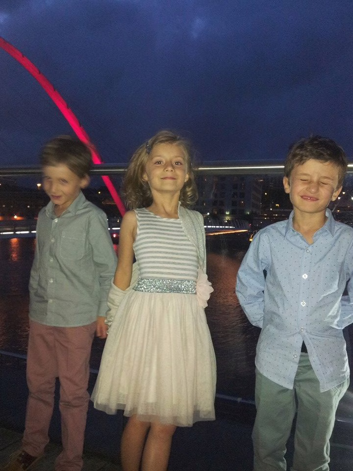 Three children standing outside with shirts untucked and generally looking messy with wild hair and untucked shirts. 